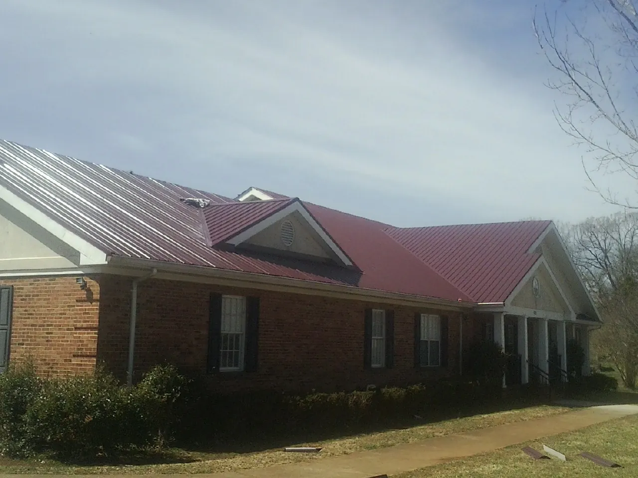 Red metal roof with gabled entries on a long brick building, from a Hail Damage Roof Repair job in Flourtown