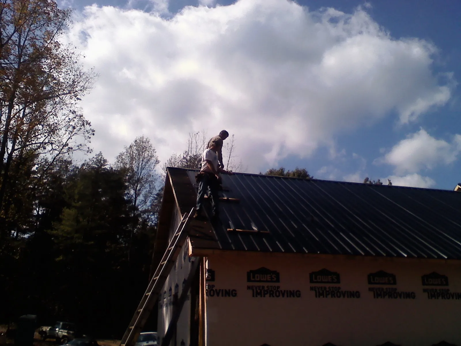 Roofer fastening dark metal panels high against a cloudy sky, from a Roof Inspection job in Flourtown